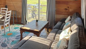 L’intérieur d’un chalet accueillant, avec un plafond en bois, un ventilateur de plafond, un canapé, une table et une vue sur l’extérieur par une fenêtre.