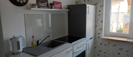 Cocina compacta con lavavajillas, estufa y ventana con vista a una casa.