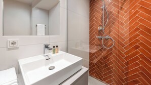 A modern bathroom with a white sink, a mirror, and a shower with a herringbone-patterned wall.