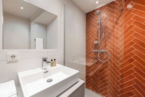 A modern bathroom with a white sink, a mirror, and a shower with a herringbone-patterned wall.