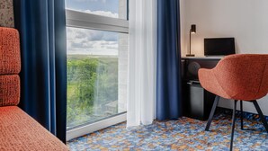 A room with a large window, a desk with a laptop, a red chair, and a patterned carpet. - Aiden by Best Western Velbert (Velbert)