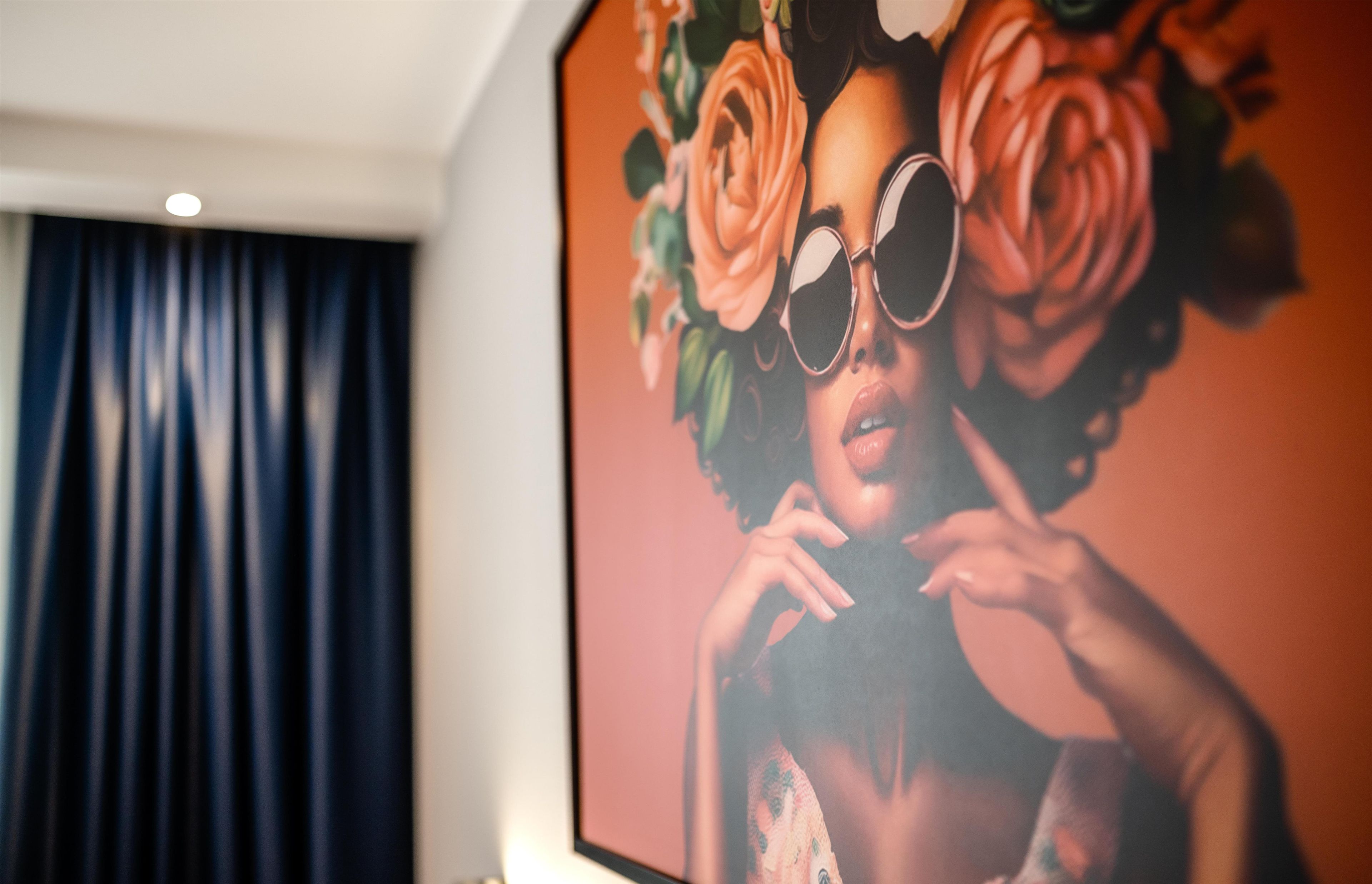 Una habitación con una gran obra de arte enmarcada en la pared, una cortina oscura y una lámpara en el techo.