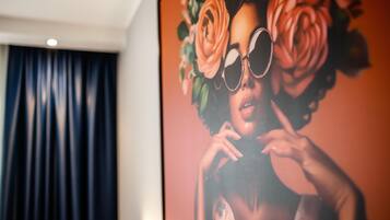 Una habitación con una gran obra de arte enmarcada en la pared, una cortina oscura y una lámpara en el techo.