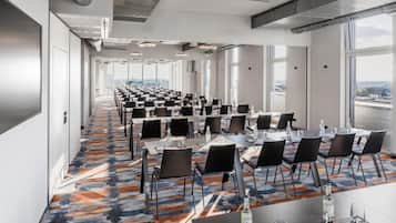 A conference room with rows of tables and chairs, large windows, and a patterned carpet.