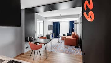 A modern hotel room with a dining area, a sofa, a TV, and a patterned carpet.