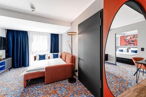 Habitación de hotel con cama, escritorio, silla, espejo y alfombra estampada.