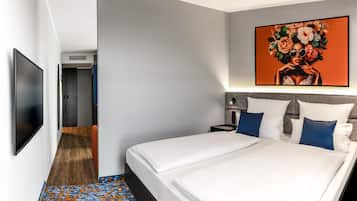 Una habitación de hotel moderna con una cama grande, un televisor de pantalla plana, un cuadro en la pared y un pasillo que lleva a otra habitación.