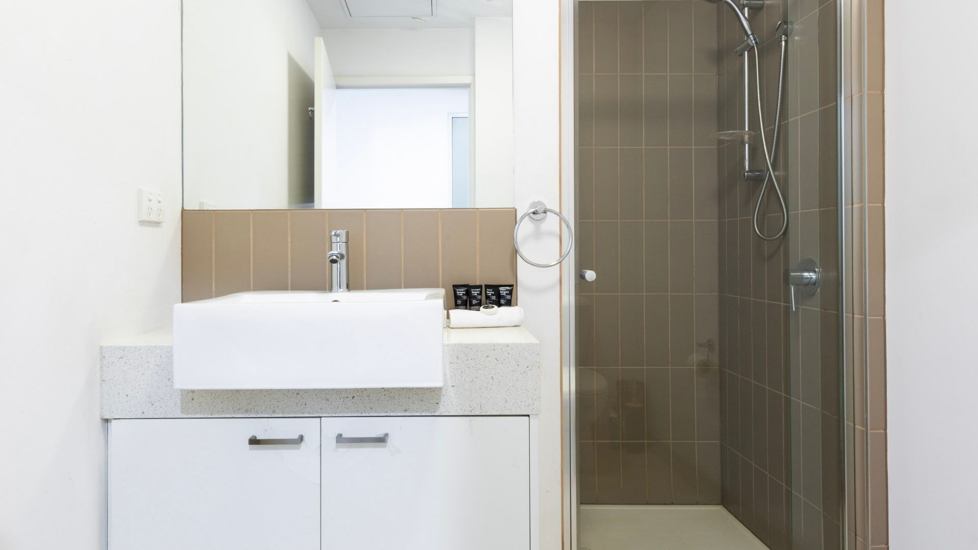 Un baño con un lavamanos blanco, un espejo, una ducha con puerta de cristal y un toallero.