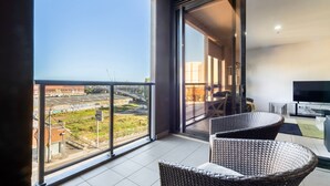 A balcony with a view of a cityscape, a dining area with wicker furniture, and a flat-screen TV. - Rowan Place Convenient Home Away With Free Parking (North Melbourne)
