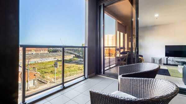 A balcony with a view of a cityscape, a dining area with wicker furniture, and a flat-screen TV.