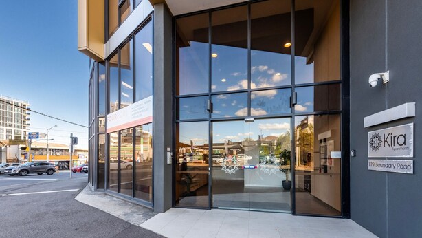 A modern building with large glass windows, a sign for 'Fourpoint' therapy services, and a 'Kira Apartments' sign on the right. - Rowan Place Convenient Home Away With Free Parking (North Melbourne)