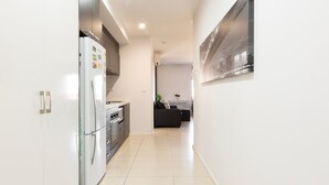 A modern kitchen with a refrigerator, oven, and microwave. There is a dining area with a black sofa and a table. - Rowan Place Convenient Home Away With Free Parking (North Melbourne)