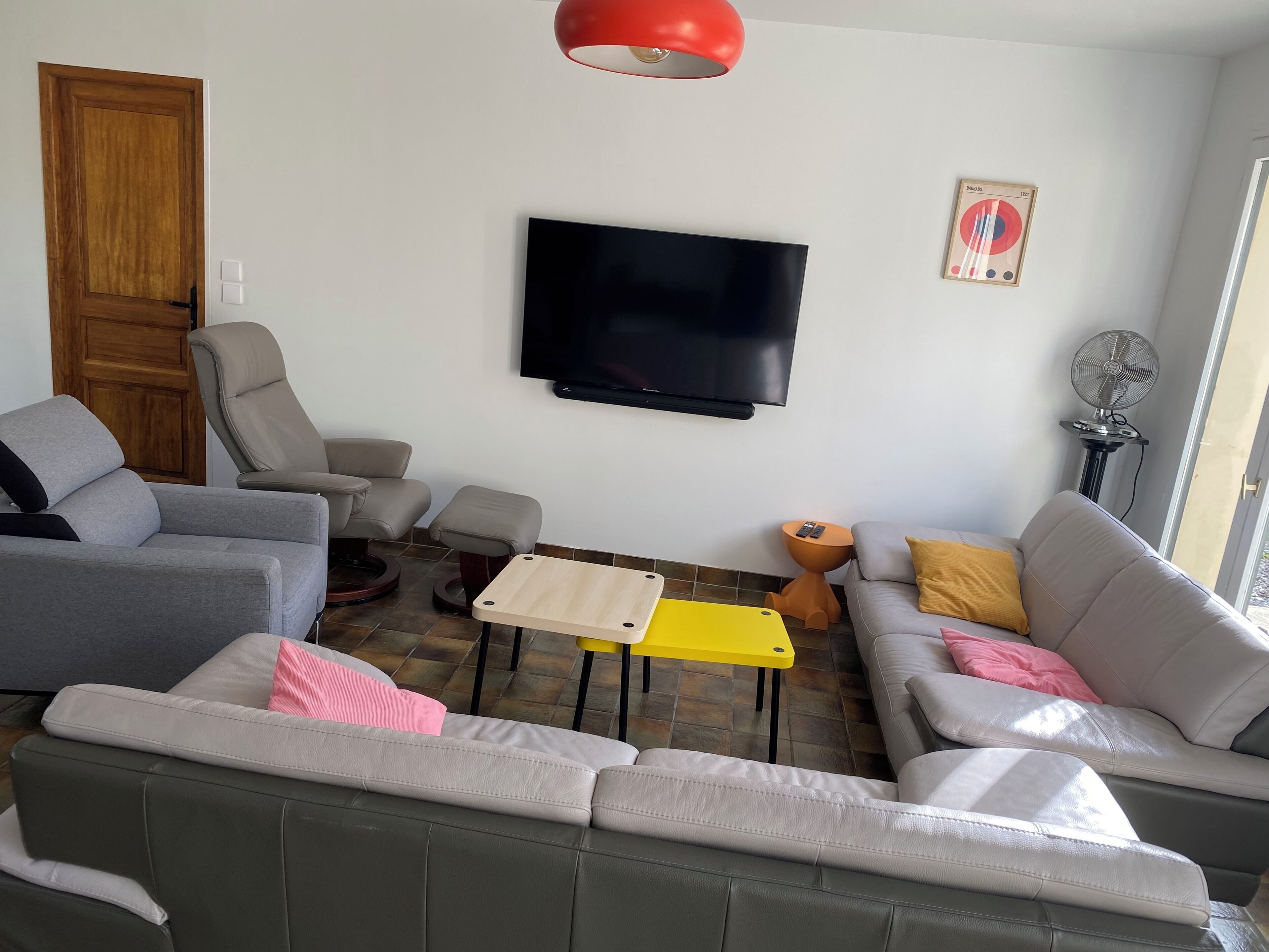 Een woonkamer met een bank, fauteuils, een salontafel, een televisie en een ventilator.