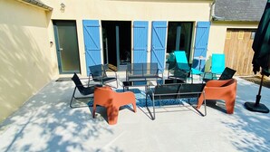 An outdoor patio with a glass table surrounded by chairs, a small round table with a chair, and a blue umbrella. - Family home in Trébeurden close to beaches and hiking trails. (Trébeurden)