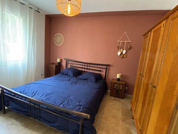 Une chambre à coucher comprenant un lit, une armoire en bois, une table de chevet, une décoration murale et un luminaire suspendu.