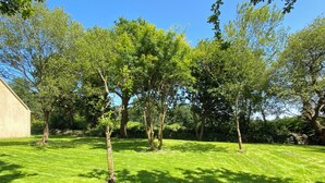 A well-maintained grassy area with several trees and a building in the background. - Family home in Trébeurden close to beaches and hiking trails. (Trébeurden)