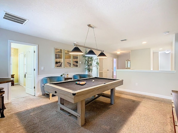 A pool table in a room with a light-colored carpet, a ceiling vent, and a hanging light fixture.