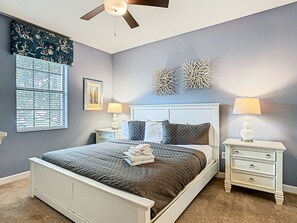 Une chambre à coucher comprenant un lit, deux tables de chevet, un ventilateur de plafond et des œuvres d’art murales.