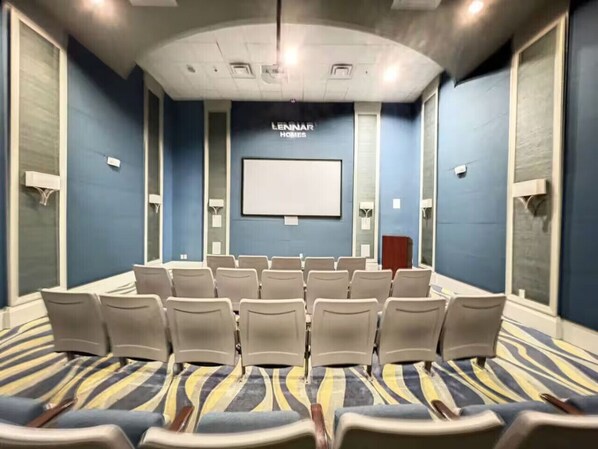 A conference room with a large screen, rows of chairs, and a carpeted floor.
