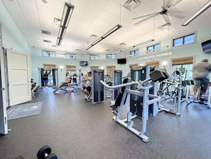 Une salle de sport équipée de divers appareils d’exercice, d’un ventilateur de plafond et d’une enseigne pour Lennar Homes.