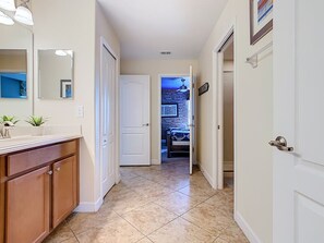 Um corredor com banheiro, uma porta que dá para um quarto e piso revestido de azulejos.