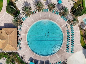 An aerial view of a circular pool surrounded by lounge chairs and palm trees.