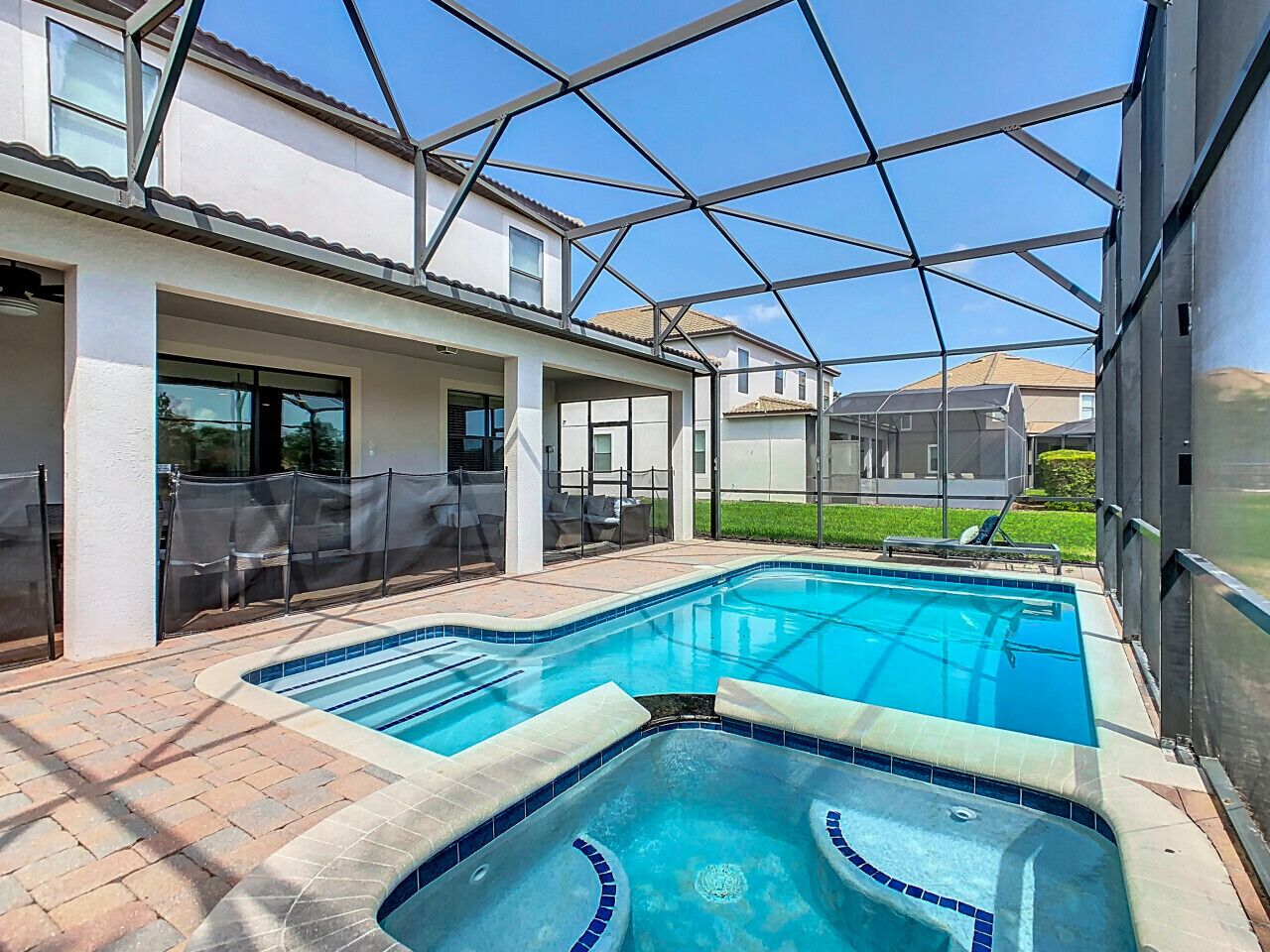 Une piscine dotée d’une enceinte en verre, entourée d’un patio aménagé avec des chaises et un espace salon couvert.
