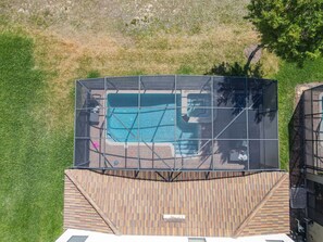 A rooftop pool with a glass enclosure, surrounded by a wooden deck and a grassy area.
