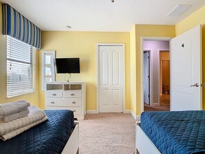 A bedroom with two beds, a dresser, a TV, and a door leading to another room.