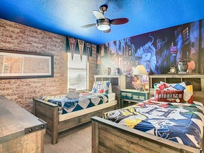 Quarto com duas camas de madeira, um ventilador de teto, parede de tijolos e um mural.