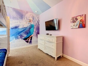 Quarto com cama, penteadeira, televisão e um mural com um personagem.