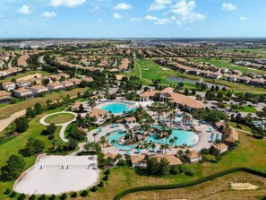 An aerial view of a resort with multiple swimming pools, a golf course, and residential areas in the background.