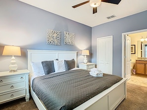 A bedroom with a bed, nightstands, a ceiling fan, and a door leading to a bathroom.