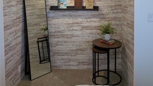 Een kamer met een grote spiegel, een kleintje tafeltje met een plant, een hanglamp en een plank met boeken en decoratieve objecten.