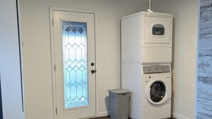 Een wasserette met een wasmachine en droger, een deur met een glas-in-lood ontwerp, en een houten vloer.