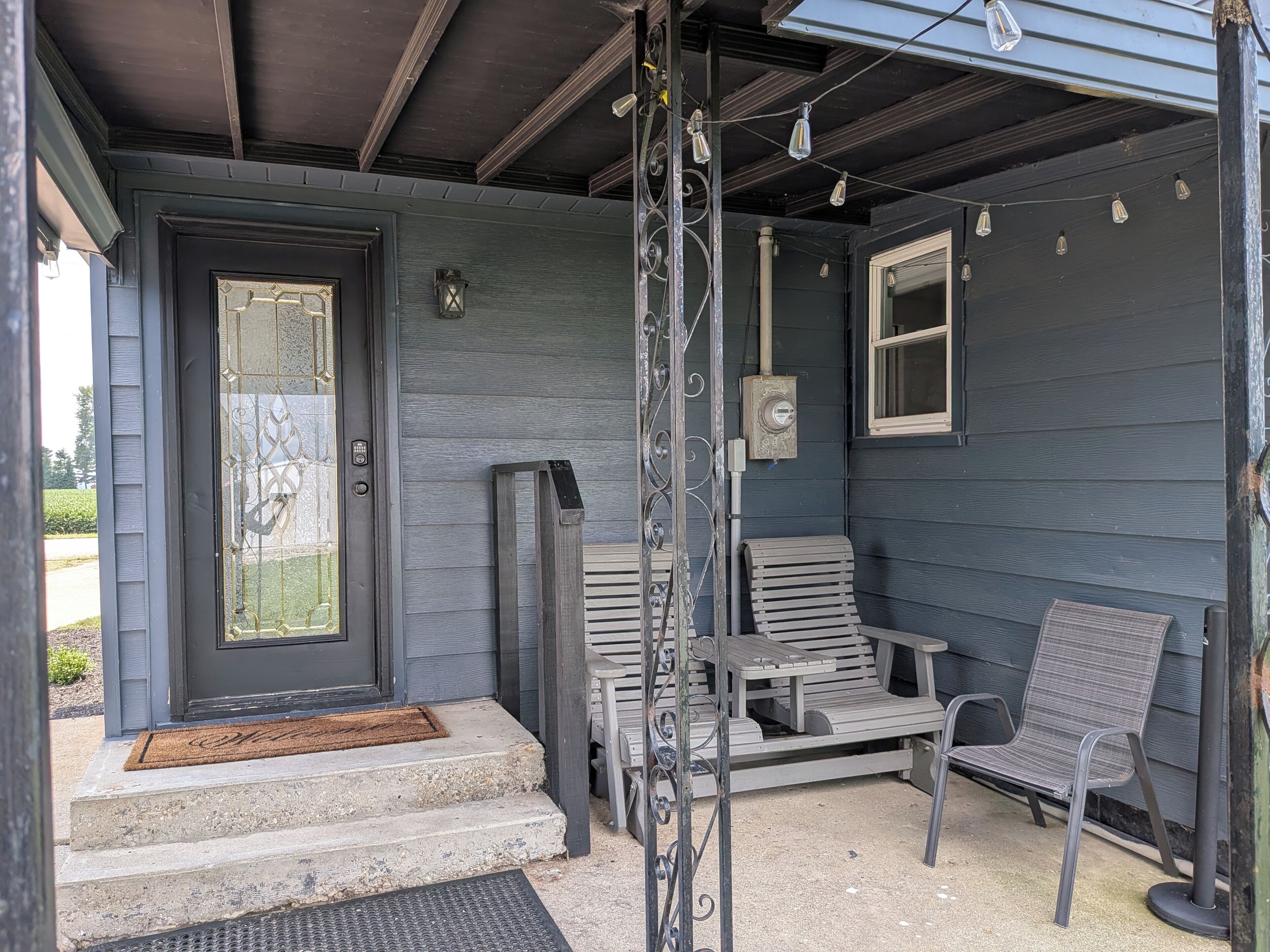A porch with a door, steps, a bench, and a chair.