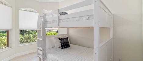 A bunk bed room with white bedding, a ceiling fan, and large windows with blinds.