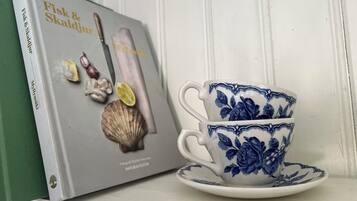 Un libro intitolato 'Fisk & Skaldjur' e una tazza blu con decorazioni floreali su uno scaffale bianco.