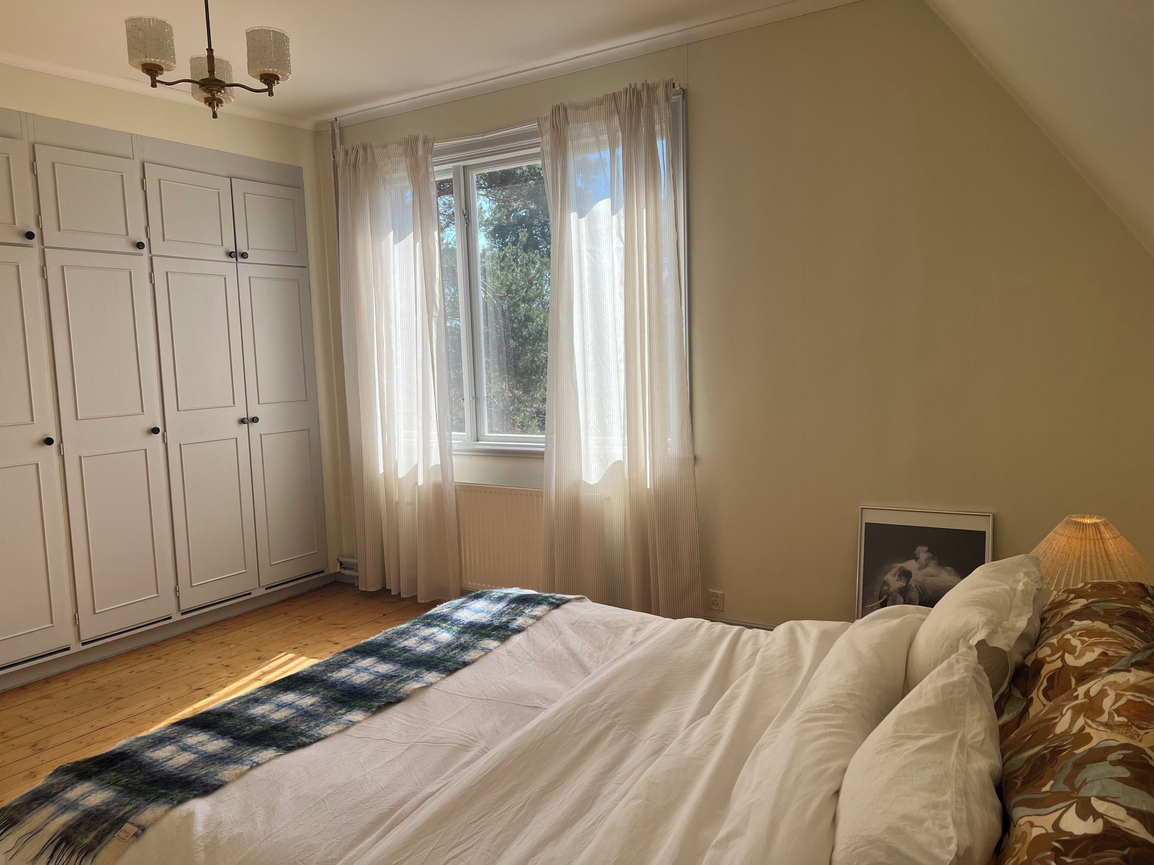 A bedroom with a bed, a window with curtains, a wardrobe, and a lamp.