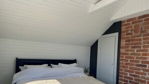 Une chambre à coucher avec un lit, des murs blancs, une tête de lit sombre et un mur en briques.