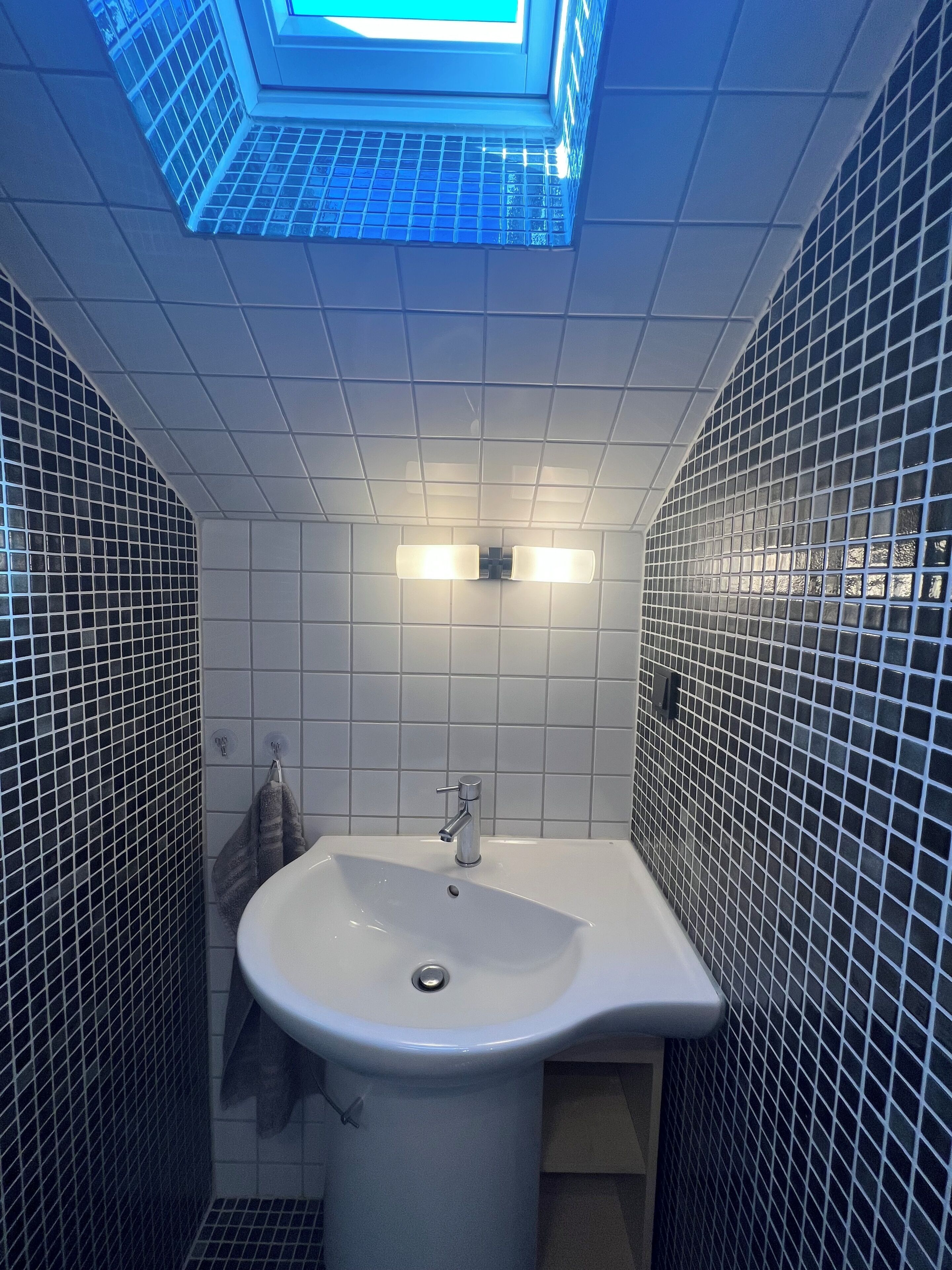 Een badkamer met een witte wastafel, betegelde wanden en een dakraam.