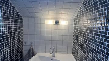 Een badkamer met een witte wastafel, betegelde wanden en een dakraam.