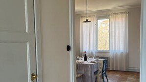 Une pièce avec une table à manger dressée pour quatre personnes, un lustre et une vue sur un bâtiment à l’extérieur.