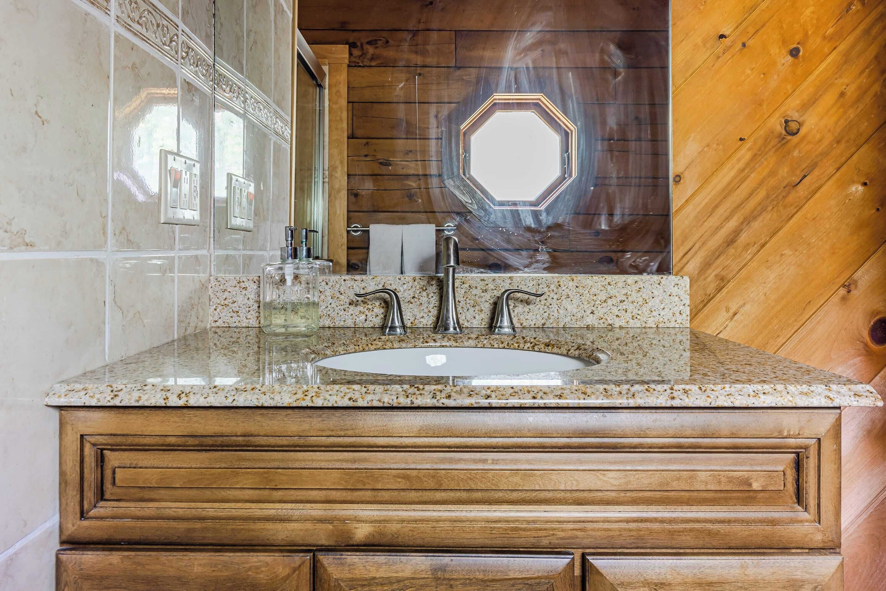 A bathroom with a wooden vanity, a marble sink, and a large mirror with a hexagonal window above it.