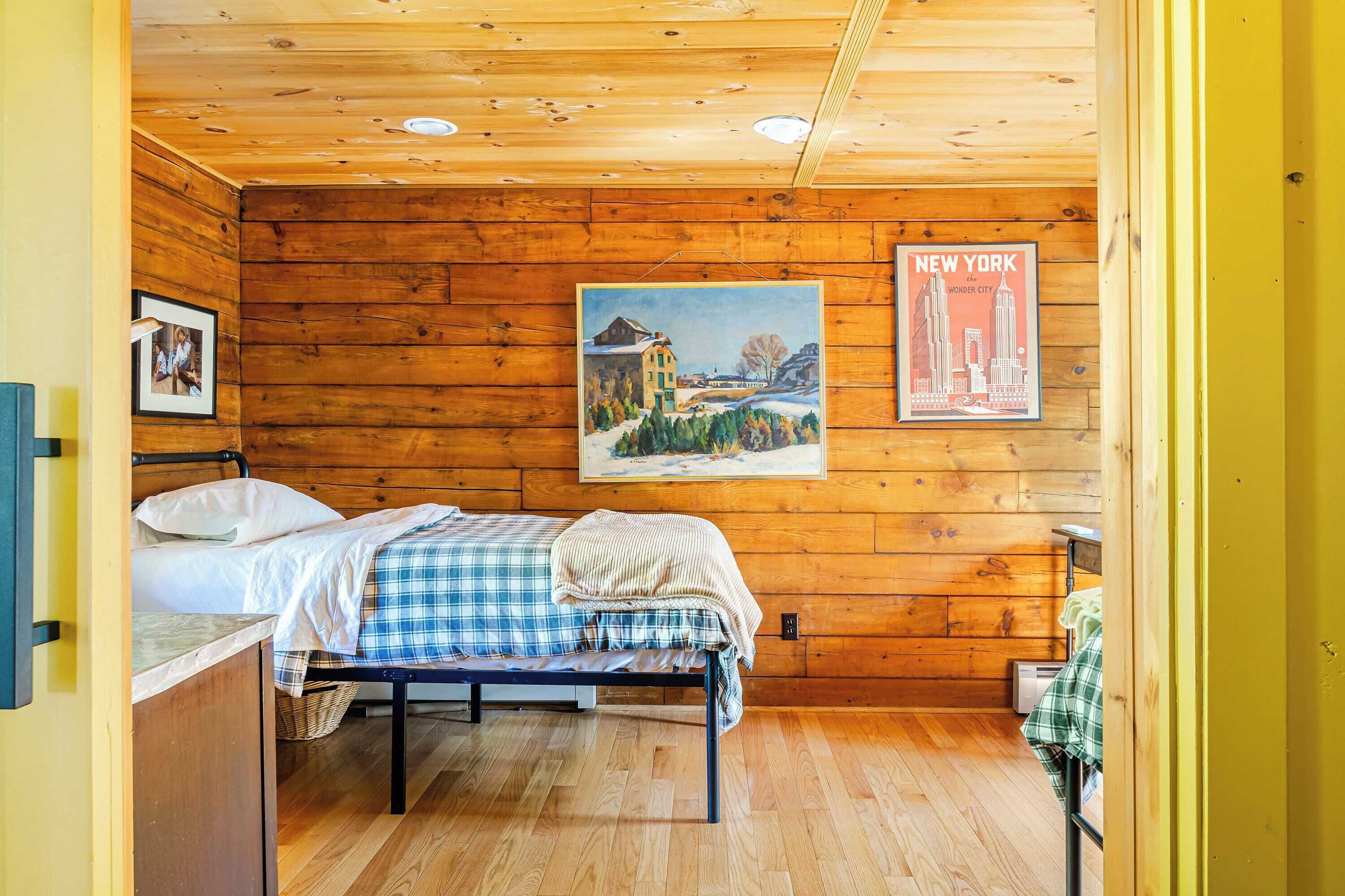 Una habitación de cabaña de madera con una cama, un cartel colgado en la pared y un cuadro enmarcado.