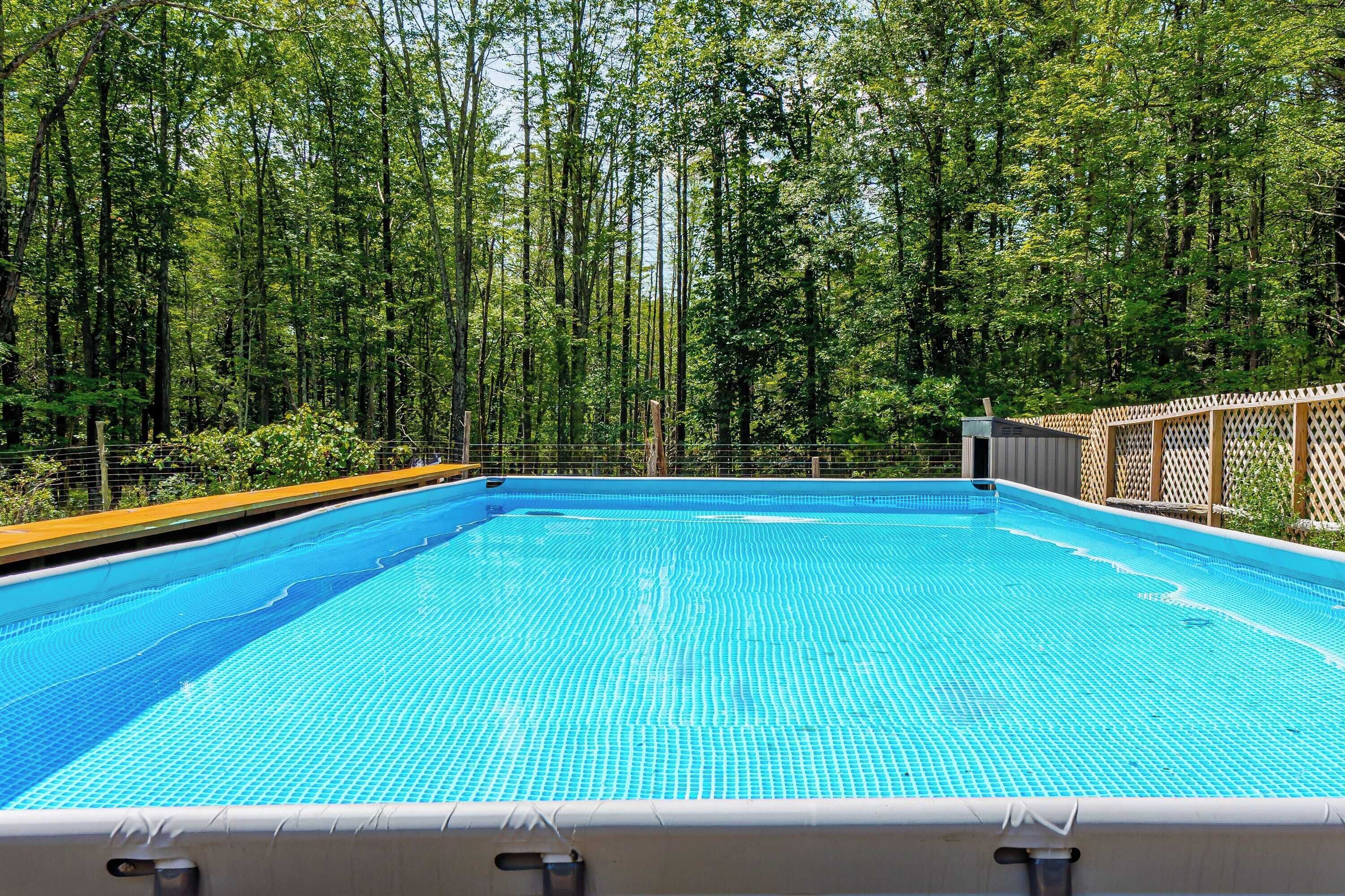 Une piscine rectangulaire dont le fond est carrelé, entourée d’une clôture en bois et bordée d’une forêt dense.