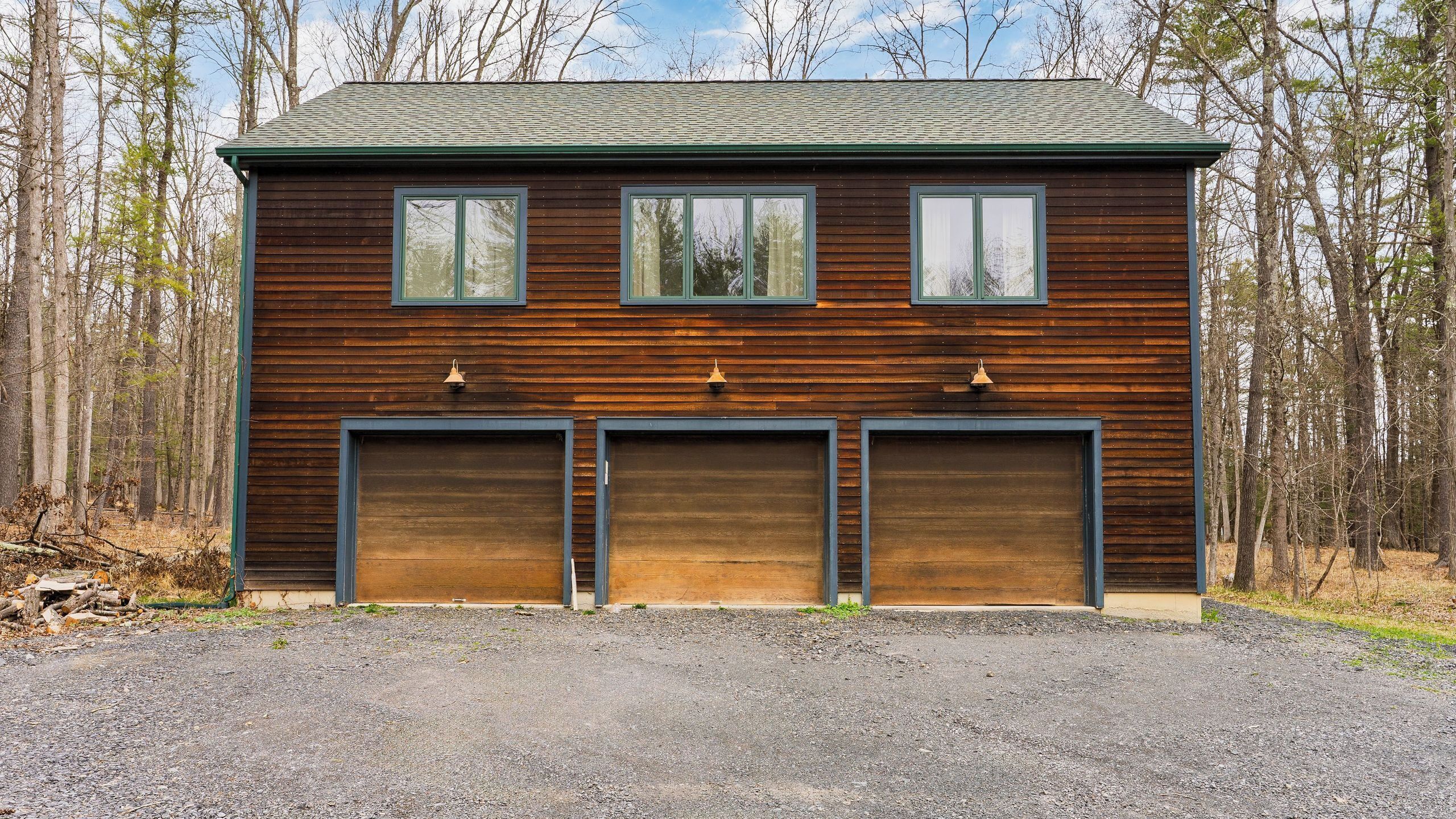 A two-story wooden building with three garage doors and a gravel driveway.