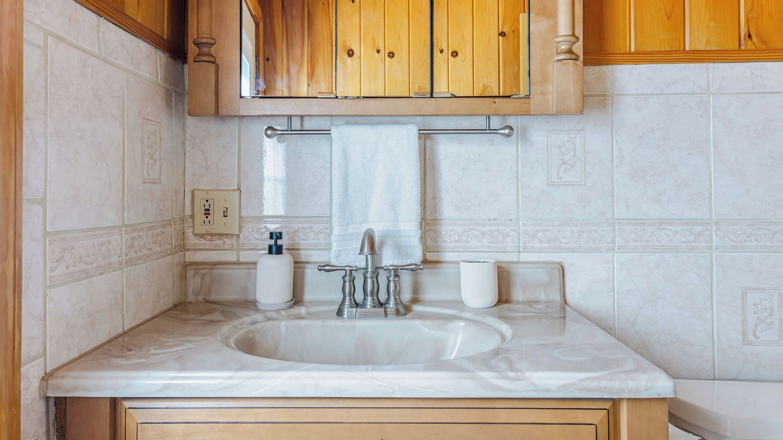 Un baño con lavamanos, armarios de madera, toallero y un salpicadero decorativo de azulejos.