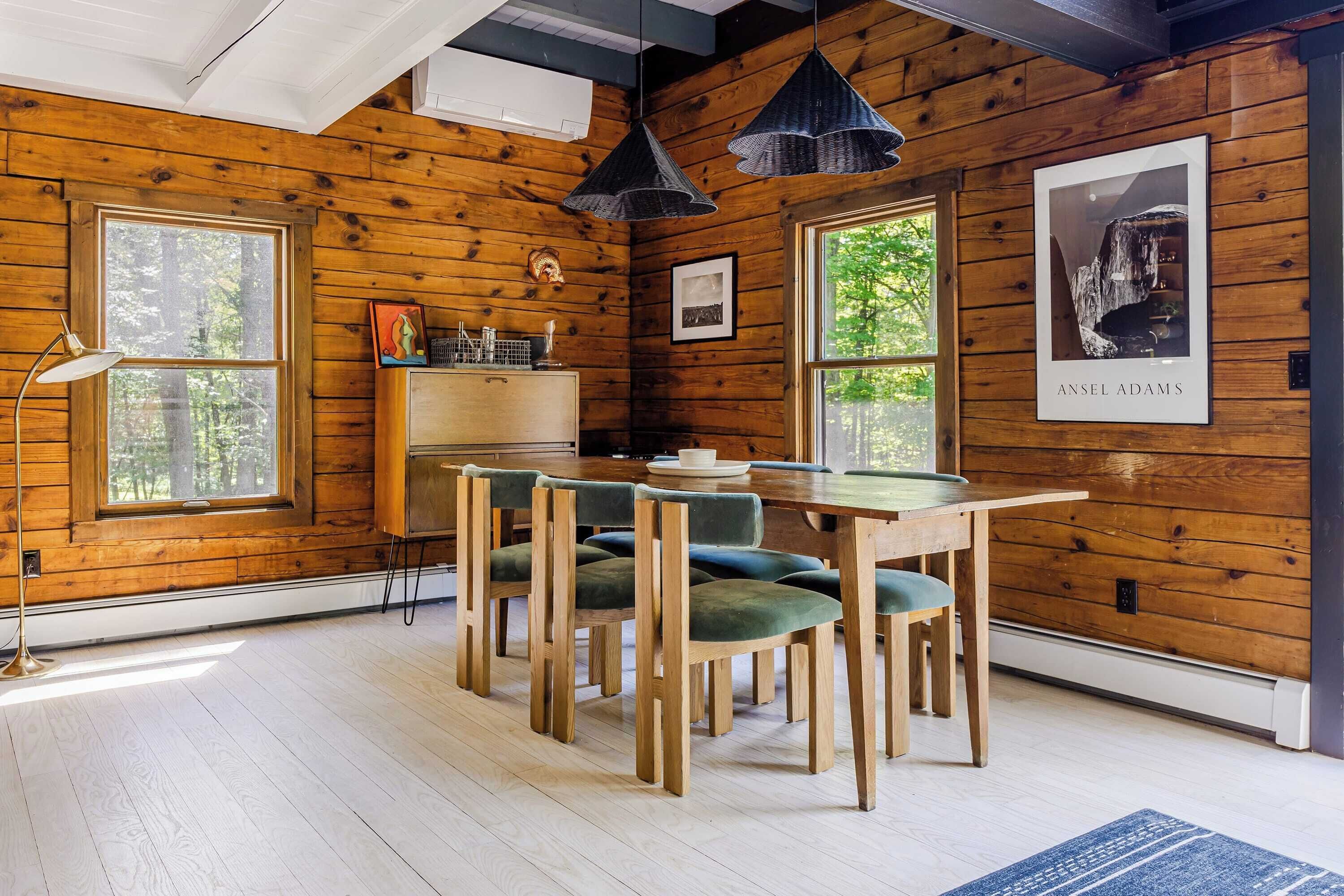 A wooden-paneled room with a dining table, chairs, pendant lights, and framed artwork.