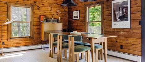 A wooden-paneled room with a dining table, chairs, pendant lights, and framed artwork.